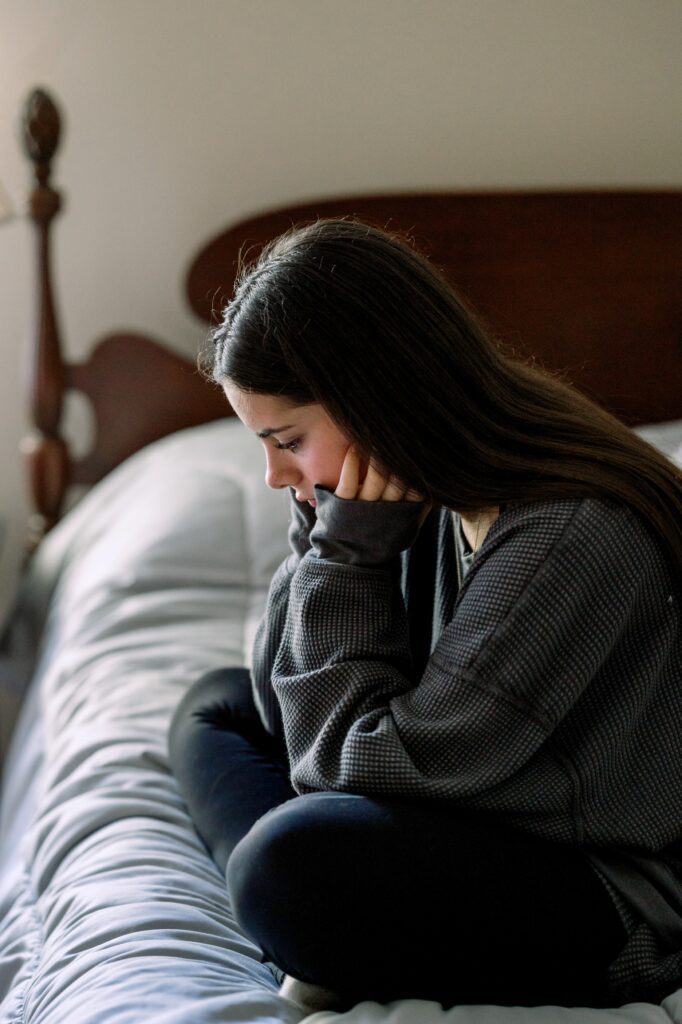 Sad woman sitting on bed with head in hands