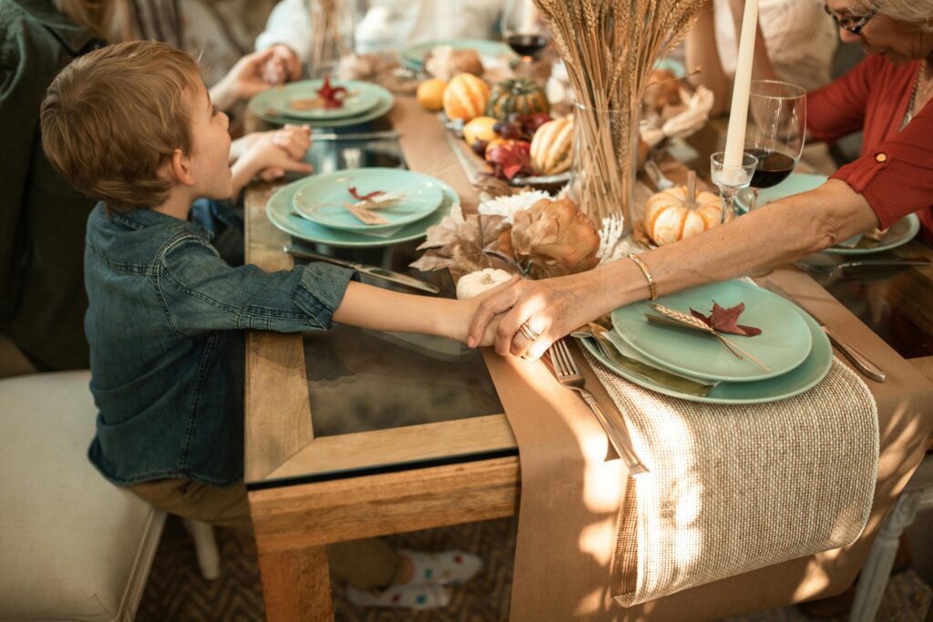 Child holding adult's hands at dinner
