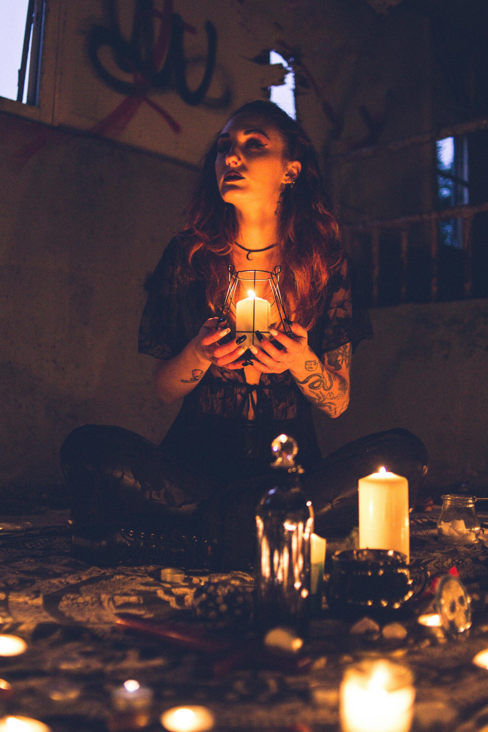 A woman holding a glowing candle in a dimly lit room where the flickering light of the candles is the only source of illumination. She appears deeply focused, as though connecting with her spiritual guide in an intimate, meditative moment.