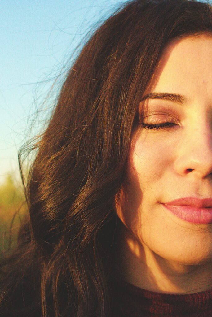 Close-up of a peaceful woman with closed eyes, basking in golden sunlight, symbolizing inner peace and spiritual reflection.